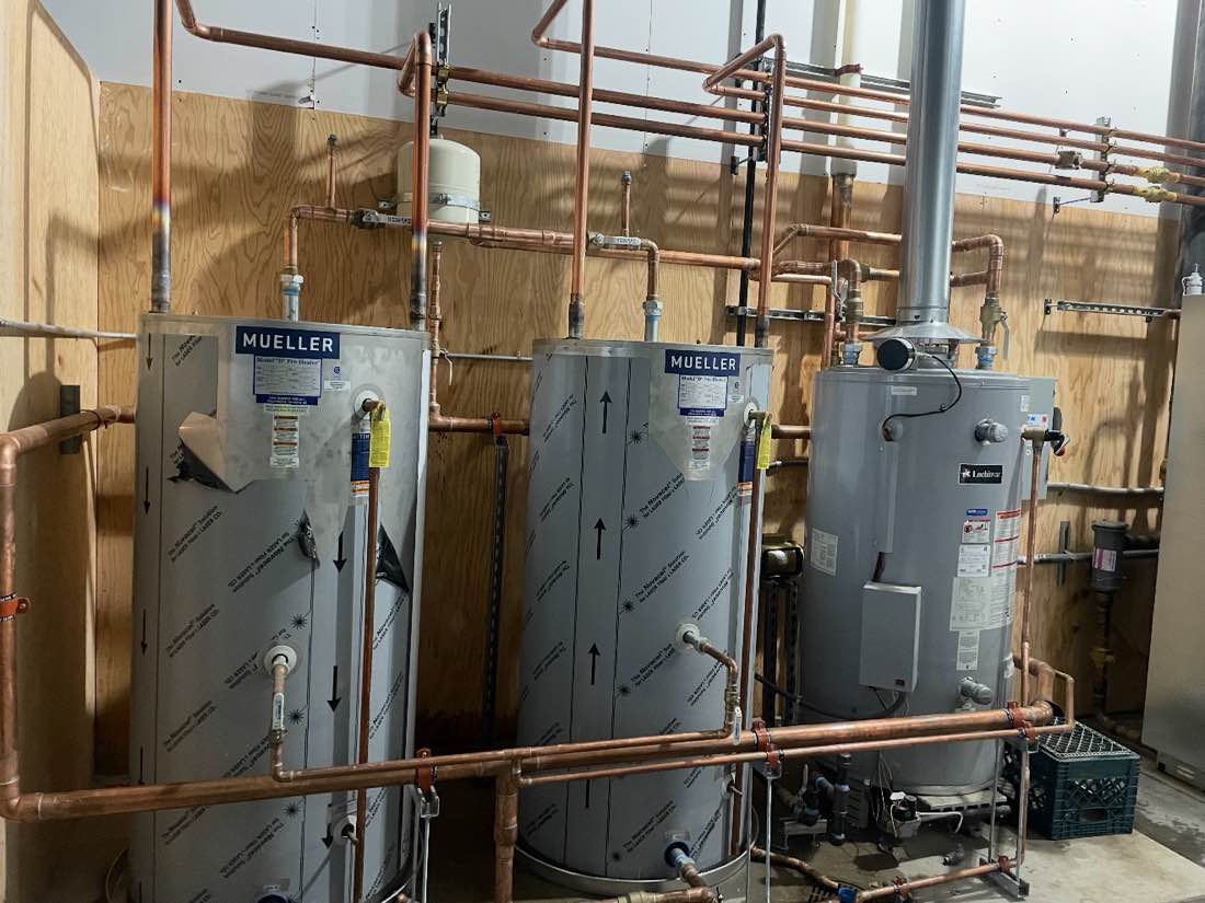 Three commercial water heaters plumbed together with a copper manifold overhead.