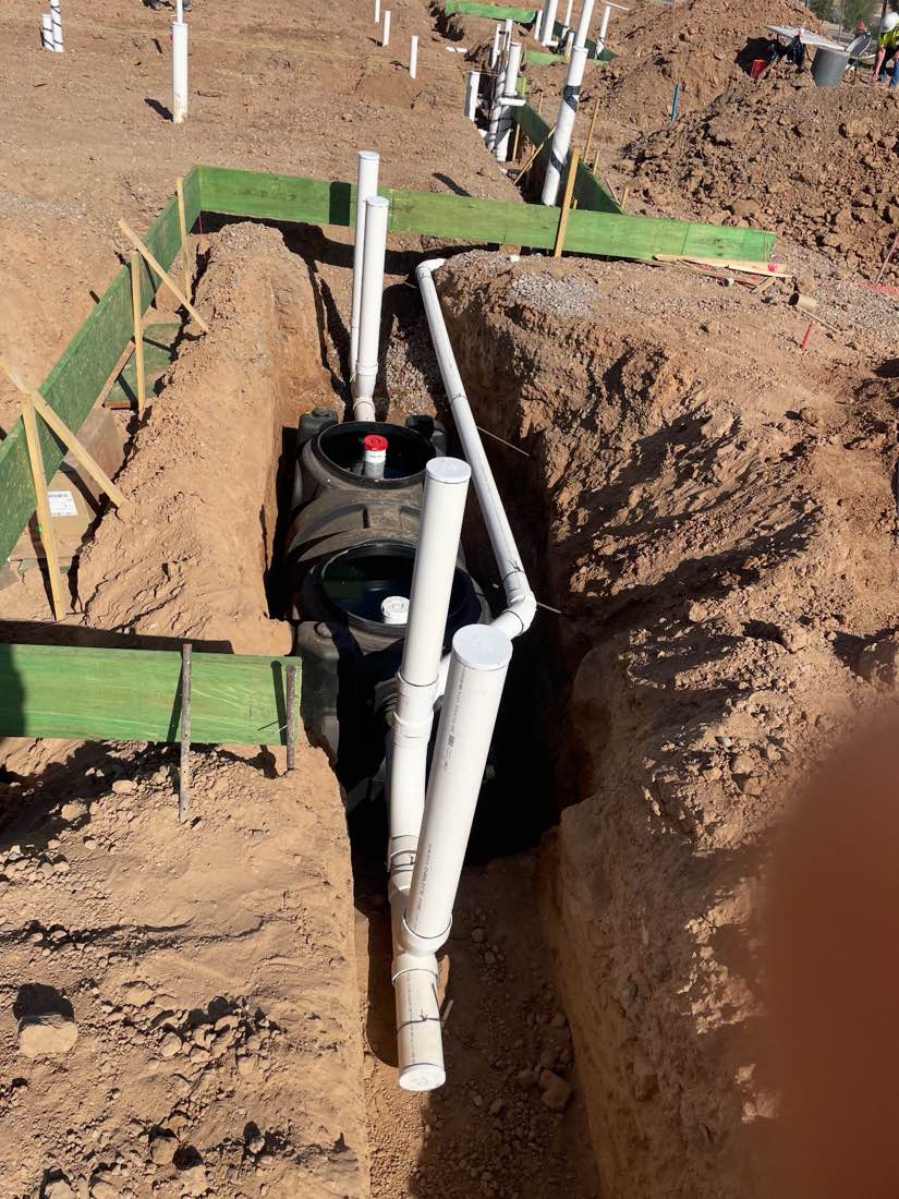 Grease interceptor tank set in a shored trench with PVC lines piped into it.