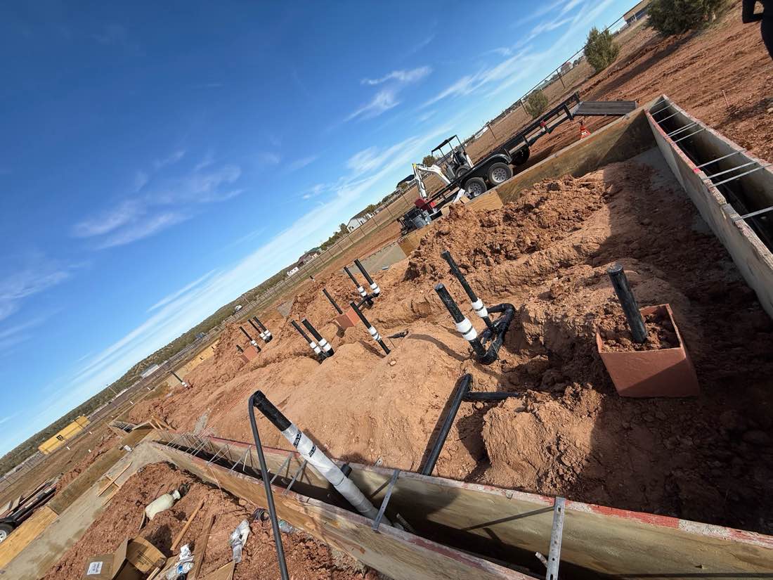 Sewer stub-ups standing in a footing trench on an open desert lot under blue sky.