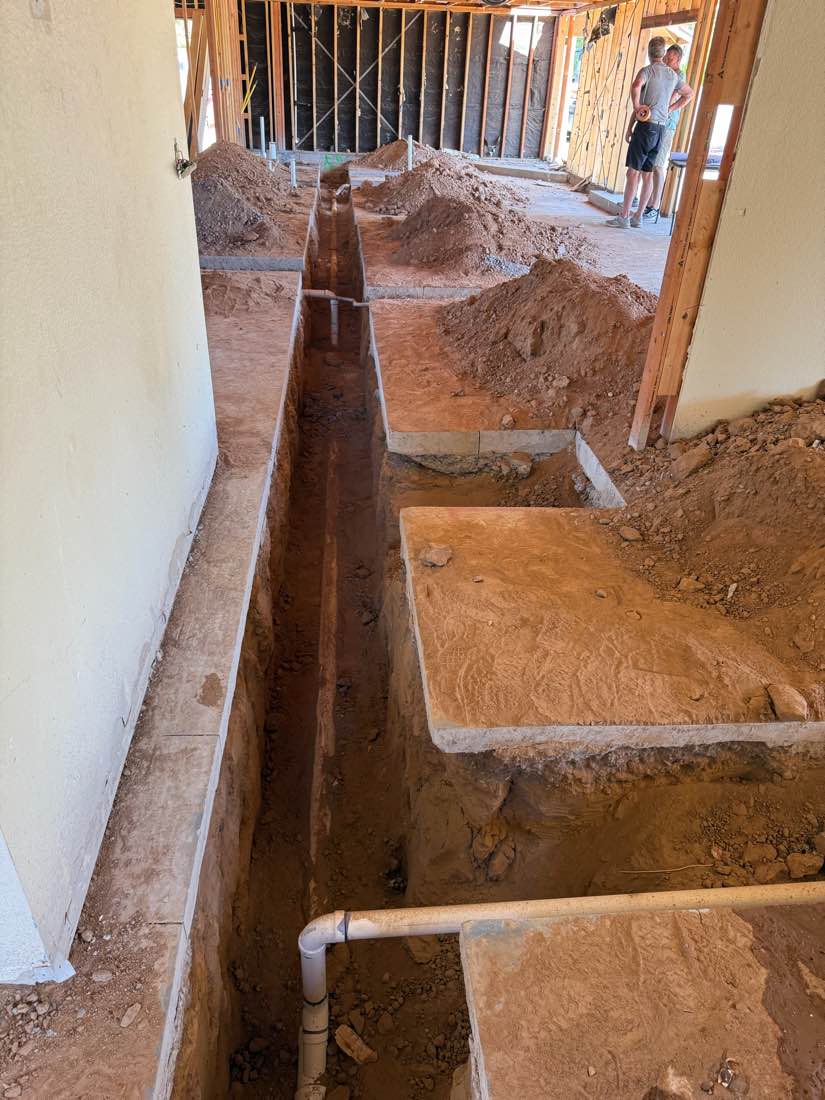 Deep trench cut through the interior of a framed building with sewer pipe running its length.