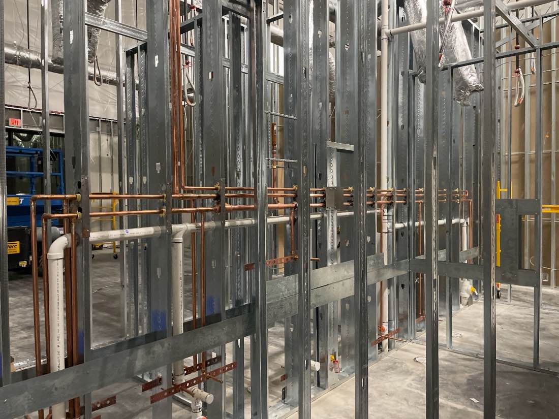 Copper supply lines and PVC waste running through metal stud framing on a commercial interior build-out.
