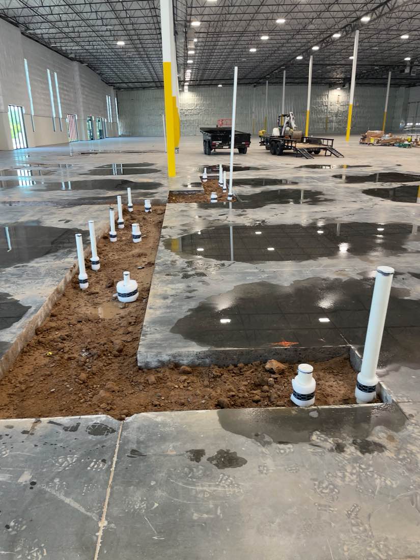 Rows of white PVC stub-ups standing in an open trench through the polished slab of a large warehouse.